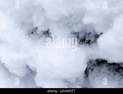 Clumps of snow on the side of a rock are viewed up close showing some of their texture and detail. Stock Photo
