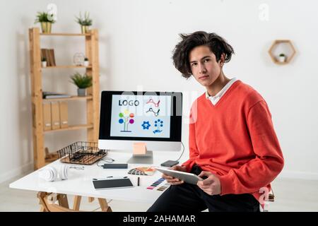 Young serious freelance designer with touchpad sitting on desk at home office Stock Photo