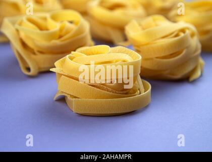 Uncooked rolled traditional italian pasta on violet background. Portion of raw fettuccine or tagliatelle or pappardelle. Dry pasta from whole wheat fl Stock Photo