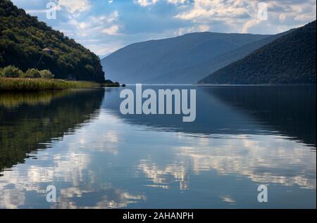 Clouds and hills reflected in the water  on Mikri Prespa lake at the village of Mikrolimni in Macedonia, Northern Greece. Stock Photo