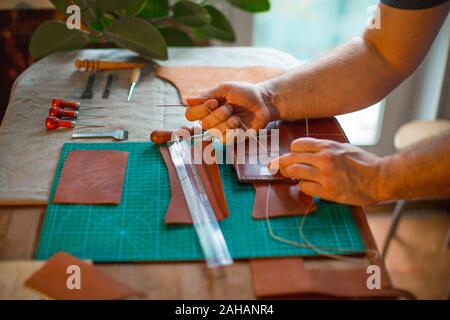 Handmade leather man making craft wallet using violet natural leather, close up photo of his hands. Handmade and craft concept Stock Photo