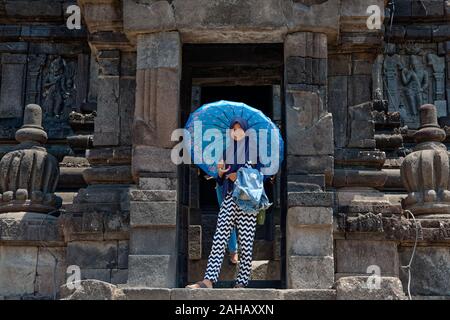 Smiling young indonesian girl wearing blue jilbab with umbrella in Prambanan temple in Java Stock Photo