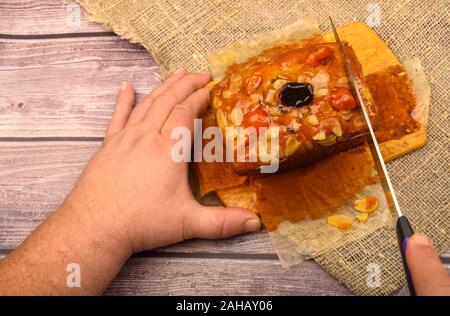 Men's hands cut home-made Christmas cake on a wooden Board on a table covered with homespun cloth Stock Photo
