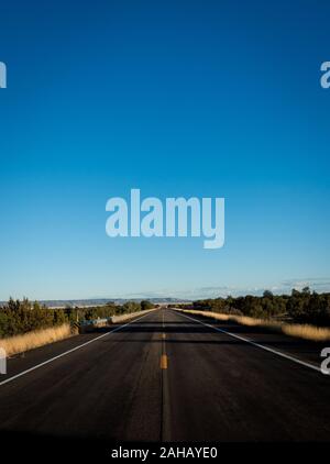 Old and lonely Route 66 in Arizona near Seligman on sunny day leading to horizon. Straight street shot of Mother Road with blue sky and shadows. Mount Stock Photo