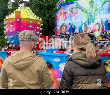 Mum and dad watching their child on a tea cup ride at a summer fair  after the Thelwall Rose Queen procession 2019 Stock Photo