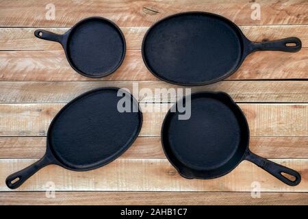 Set of four round and oval cast iron skillets of different sizes on a wooden background. Viewed from above on a rustic wooden table background. Stock Photo