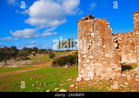 Ruined corner of old stoned house without roof. Green field, trees, dirt country road and blue sky with white clouds. Sunny autumn day in Seville, Spa Stock Photo