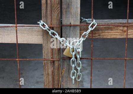 Closed improvised warehouse wooden doors with rusted metal net locked with padlock on strong chain at abandoned military complex with concrete floor Stock Photo