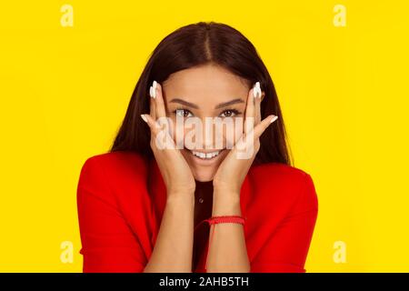 Natural woman with no makeup multicultural looking smiling happy touching face with both hands. Mixed race model isolated on yellow background with co Stock Photo
