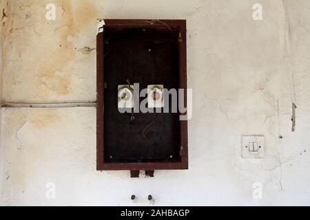 Two old vintage retro disconnected ceramic fuse holders with missing fuses inside wooden box on dilapidated cracked wall next to plastic light switch Stock Photo