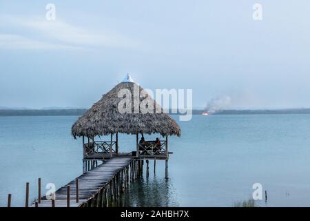 Dock at lake Itza in the blue hour with wild fire in the back, El Remate, Peten, Guatemala Stock Photo