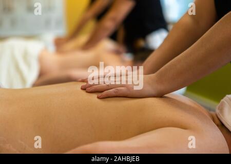 Students practice effleurage rubbing techniques in the classroom, hands of a pupil are seen on the back of a volunteer during exam preparation Stock Photo