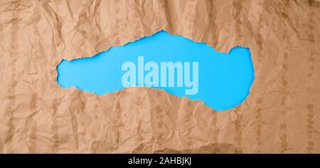crumpled paper texture from a brown sheet of paper with greasy spots and a large hole. abstract banner for the designer, blue backdrop. Stock Photo