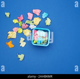stationery blue metal bucket filled with crumpled multi-colored stickers, top view, blue background Stock Photo