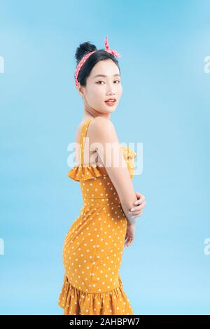 Beautiful young smiling woman wearing polka-dot dress. Model posing near blue wall in studio. Positive female Stock Photo