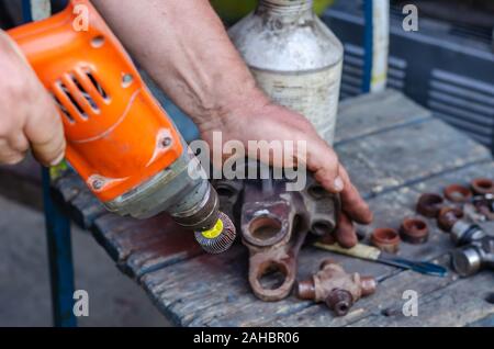 A man using an electric drill polishes the seats of the driveshaft bearings. Replacing worn parts with new ones. Auto repair. Horizontally. Soft focus Stock Photo