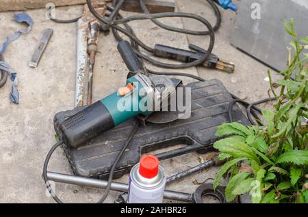 Grinder, welding, pipe wrench and other hand tools on the concrete floor next to the workshop. The process of self-repairing a car. Selective focus. Stock Photo