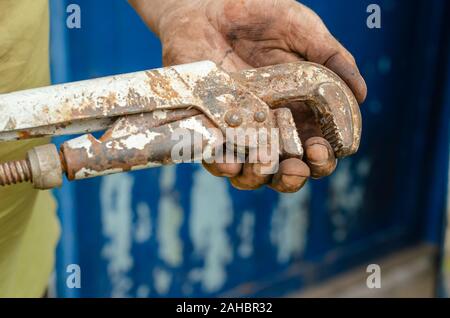 Old vintage pipe wrench in dirty worker hand. Close-up. Eye level shooting. The horizontal location of the photograp Stock Photo