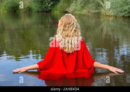 Young blonde woman in red wrap walking in natural water Stock Photo