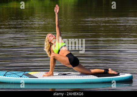 Young european woman in triangle pose on floating paddle board Stock Photo