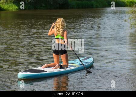 Kneeling young european woman paddling with paddle board on water of river Stock Photo