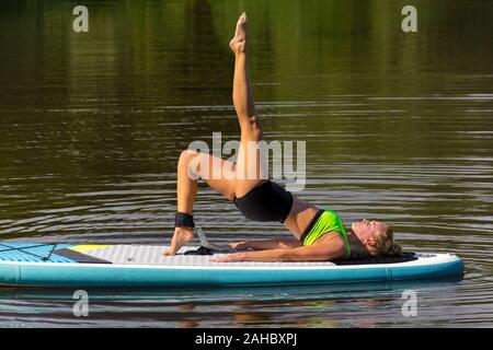 Young caucasian woman in yoga posture with leg up on paddle board Stock Photo