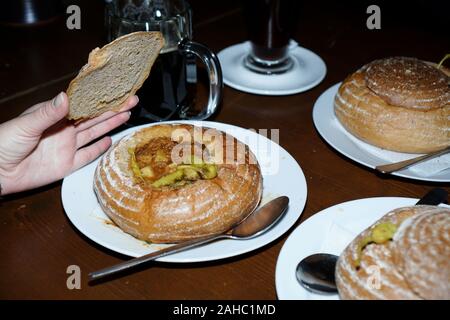 Goulash served in a bread bowl on a white plate. Restaurant in the Czech Republic. Czech cuisine. Hand lifts a lid of bread Stock Photo