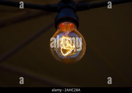 A single electric light bulb lit hanging from the ceiling Stock Photo