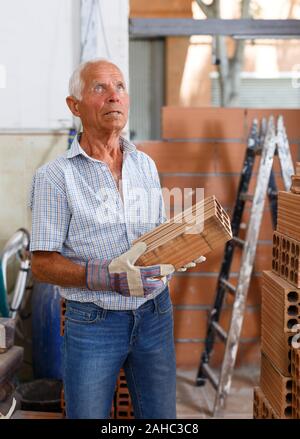 Skillful older man inspecting brick for installing wall in building under construction Stock Photo