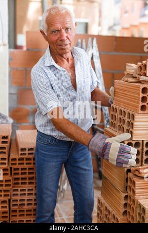 Skillful older man inspecting brick for installing wall in building under construction Stock Photo