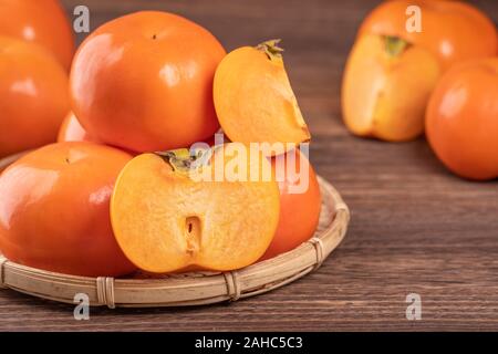 Fresh, beautiful orange color persimmon kaki on bamboo sieve over dark wooden table. Seasonal, traditional fruit of Chinese lunar new year, close up. Stock Photo