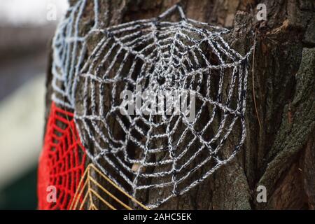 Knitted cobweb of colored threads on a tree trunk, close-up. Stock Photo