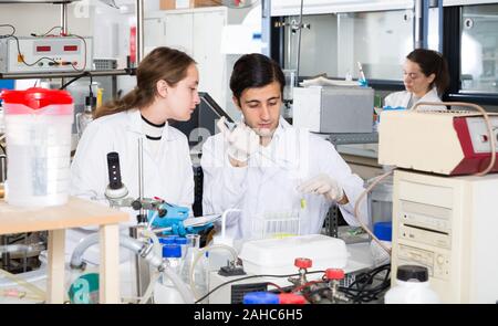 Two nice lab technicians discussing while working with reagents in test tubes during chemical experiment Stock Photo