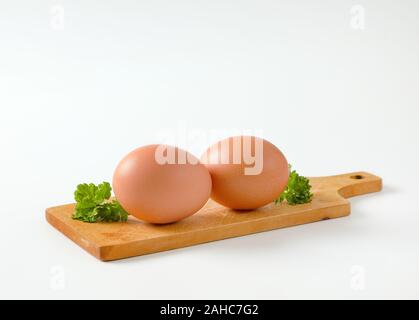 Two brown eggs on wooden cutting board Stock Photo