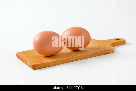 Two brown eggs on wooden cutting board Stock Photo