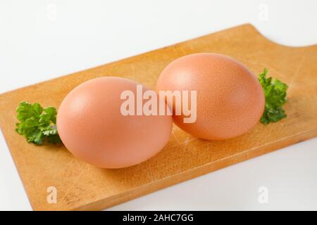 Two brown eggs on wooden cutting board Stock Photo
