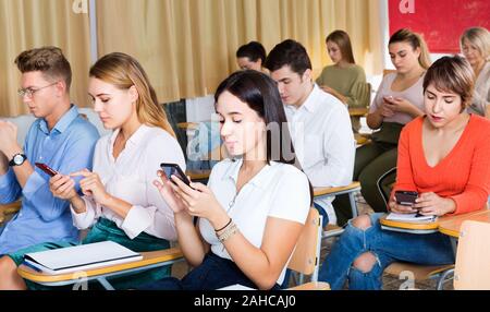 Diligent students using smartphones to find necessary information on lecture in university class Stock Photo