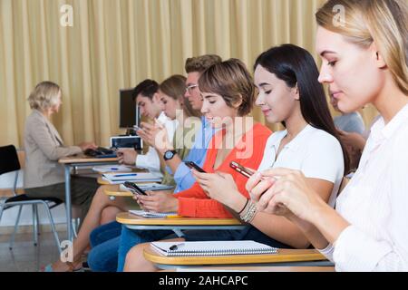 Students using smartphones to find necessary information on lecture in university class Stock Photo