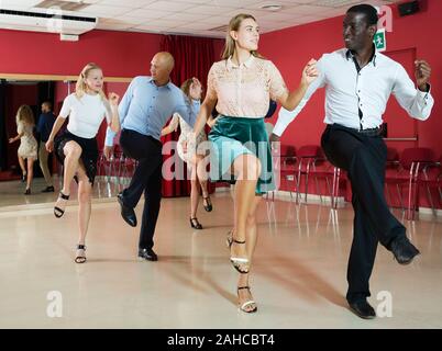 Young smiling people practicing vigorous jive movements in dance class Stock Photo