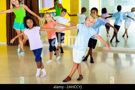 Group of glad  cheerful children practicing vigorous jive movements in dance class with female coach Stock Photo