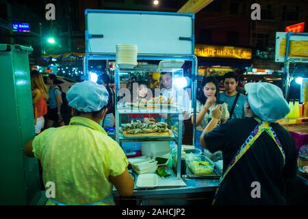 Bangkok/Thailand-December 2019: Two women wearing hair nets selling their food at their food stall at night in Chinatown with customers deciding in th Stock Photo