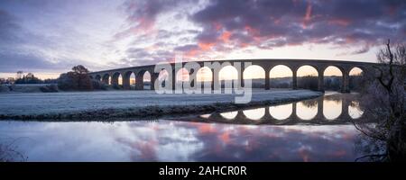 A vibrant sunrise fills the sky behind Arthington Viaduct in Lower Wharfedale, Yorkshire, reflected in the calm waters of the River Wharfe. Stock Photo