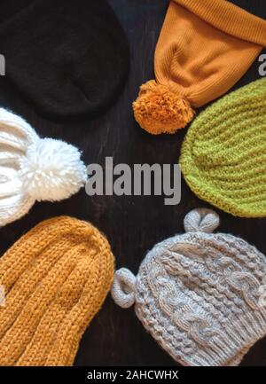 Different types of knitted hats yellow, green, white, gray on a dark wooden background with copy space. View from above Stock Photo