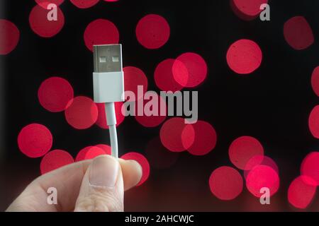 Hand holds a USB cable charger in front of red bokeh Stock Photo