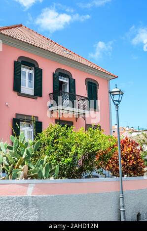 Ribeira Brava, Madeira, Portugal - Sep 9, 2019: Traditional house in Madeiran city. Building with a pink facade and a beautiful garden with colorful flowers and bushes. Sunny day. Vertical photo. Stock Photo