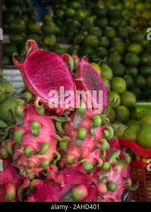 Fresh and beautifully arranged pink dragon fruits (entire and cut) with various mangos in the background at Vietnamese fruit market, portrait frame Stock Photo
