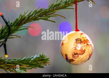 Single hand-made bauble hanging on the branch of a Christmas tree with out of focus fairy lights in the background