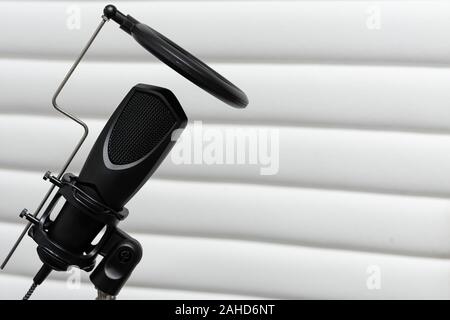 Condenser microphone placed on a tripod with white acustic panels in the  background in a music studio, ready for recording. Stock Photo