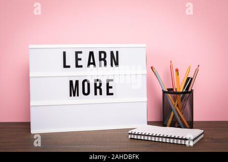 Learn More. Education, skills, courses and career opportunities concept. White lightbox on a wooden table.. Stock Photo