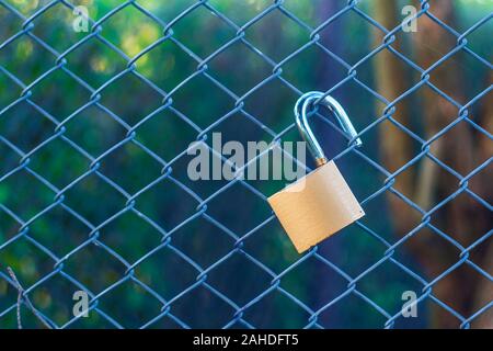 Open a bit rusty padlock hanging on fence wire netting with copy space Stock Photo